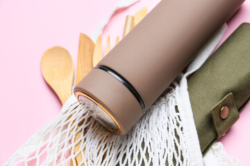 Mesh shopping bag with modern thermos and cutlery on color background, closeup