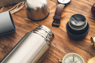 Modern thermos and items for travel on wooden background, closeup