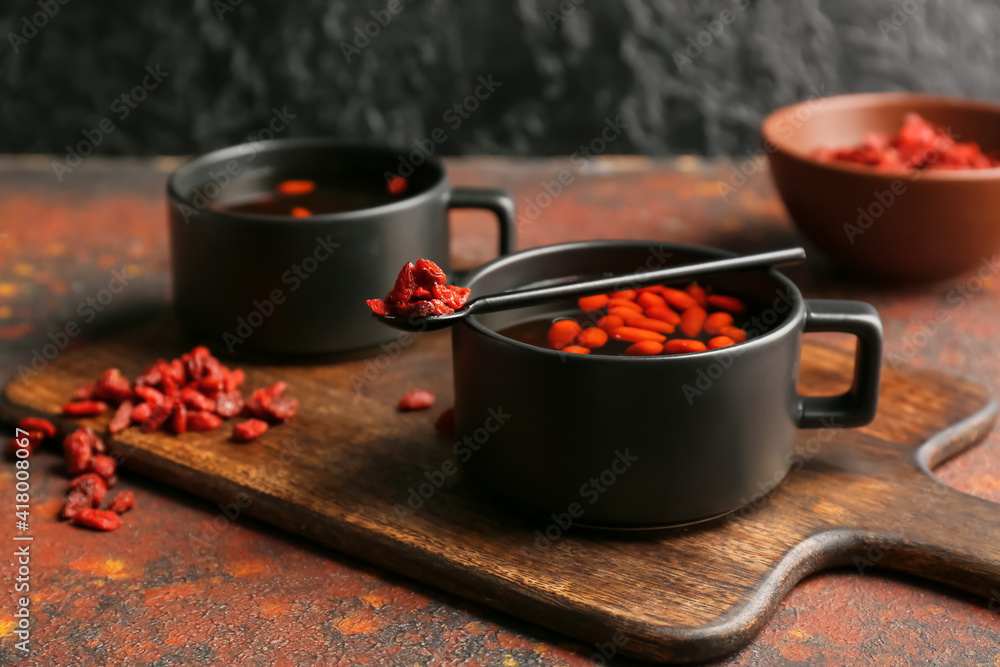 Cups of hot tea with goji berries on grunge background