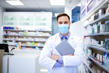 Wall Mural - Portrait of pharmacist in protection mask holding tablet computer and standing in pharmacy shop.