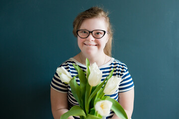 Wall Mural - Portrait of teenage girl with Down syndrome standing with flowers on blue background. Disability children. World Down syndrome day.