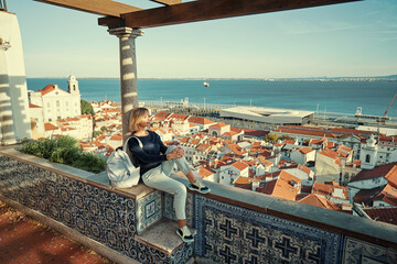 Traveling by Portugal. Young traveling woman enjoying old town Lisbon view, red tiled roofs, ancient architecture and river.