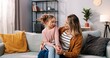 © VAKSMANV - Portrait of Caucasian cheerful cute family mom and little daughter kid at home chatting having conversation while sitting on couch in modern living room, mom and child spending time at home together
