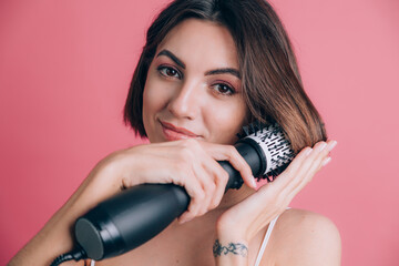 Women on pink background hold round brush hair dryer to style hair