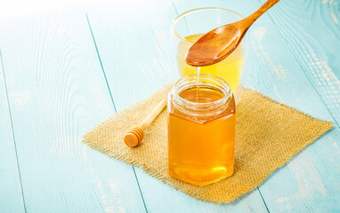 Sticker - Closeup of golden honey pouring from a wooden spoon into a jar next to a juice glass