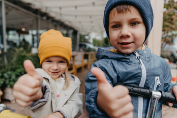 Wall Mural - portrait of little brother and sister who went for a walk together in the autumn city. Together they show a thumb that symbolizes their joy