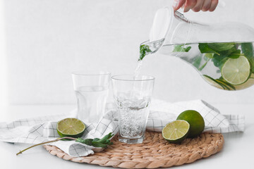 Wall Mural - Detox water with lime fruit. Hand pouring lime fruit water from jug into glasses