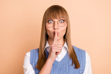 Wall Mural - Photo portrait of female student keeping secret finger near lips staring spectacles isolated on pastel beige color background