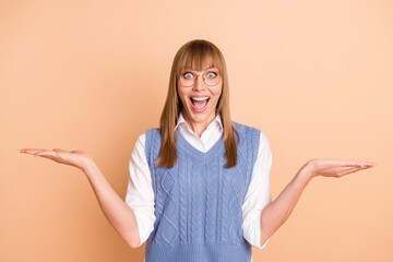 Wall Mural - Photo portrait of amazed shocked girl in spectacles holding empty space on hands staring isolated on pastel beige color background