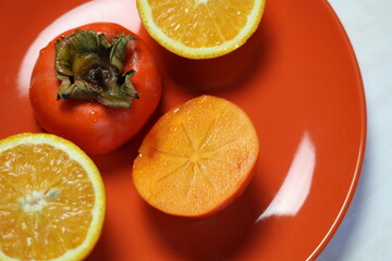 Wall Mural - fresh orange fruit and persimmon halfs on orange plate 