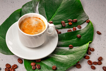 Wall Mural -  Cup of hot black coffee and coffee beans on monstera leaf close up