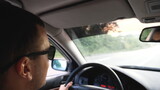 Fototapeta  - Unrecognizable man in sunglasses driving car on highway. Young confident guy looking to road during controlling auto. Back view from vehicle salon. Concept of road trip. Slow motion