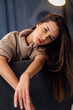 © Misha - A beautiful young girl is sitting on the back of a chair. The girl is wearing a brown cozy sweater. Her hand straightens her thick, wavy hair.