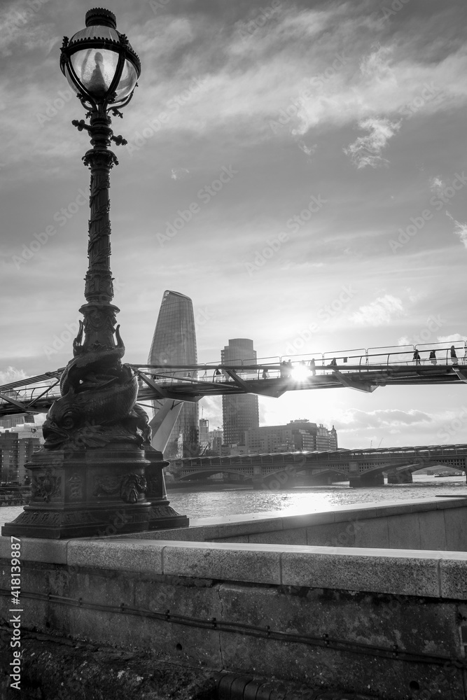Czarno-białe pionowe ujęcie kładki dla pieszych Millenium Bridge w Londynie o zachodzie słońca - obrazy, fototapety, plakaty 