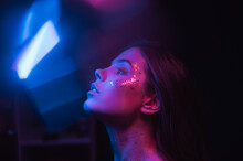 Blurred night art portrait of a woman in neon. Portrait of a skinny brunette with glitter on her face in purple and blue light, looking to the side and glare