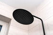 A modern, black metal shower with a large rain shower, placed on tiles.