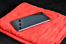 On A Red Background Lies A Black Phone In The Glass Of Which There Is A Reflection. High Quality Photo