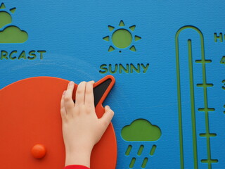 Kid's hand moving the arrow of a weather wheel