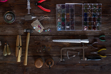 Jeweler's tools lying on wooden table, hand made flat lay for artisan with beads, gems, anvil, pliers, side cutters, hammer, hand vise, crossbar