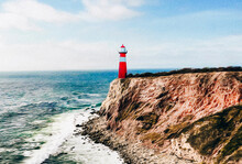A Red And White Lighthouse On The Edge Of A Cliff By The Sea. 