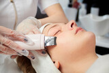 Fototapeta Tęcza - Close-up of the face of a woman who is doing an electronic peeling in gloves. Beauty salon.