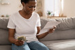 No money left. Depressed sad Black girl holding last cash money and papers calculate domestic bills at home. African woman frustrated about lack of finances, feeling anxiety about debt or bankruptcy.
