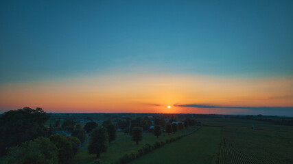 Wall Mural - An Aerial View of a Sunset over Green Farm Lands with a Reddish Sky