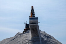 A Stockpile Of Salt Or Sodium Chloride Road Salt, Rocksalt Stockpiled For Winter Snow And Ice Deicing Controls. The Road Salt Is Pilled In One Mound With An Excavator On Top Of The Pile Sorting Salt.