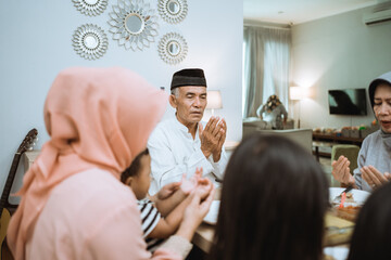 happy asian muslim family praying before having their iftar meal during ramadan fasting