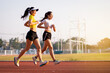 © EduLife Photos - Two young Asian women in sports outfits jogging on running track in city stadium in the sunny morning to keep fitness and healthy lifestyle. Young fitness women run on the stadium track