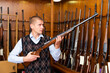 © JackF - Confident male hunter examining hunting shotgun before buying in gun store.