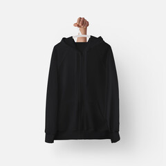 Black textured hoodie template with zipper, pocket hanging on a plastic hanger in hand, front view for design presentation, print.