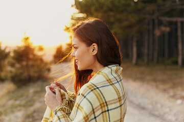 Joyful traveler on a path in the forest with a plaid blanket on her shoulders