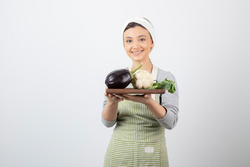 Wall Mural - A young cute woman model holding a wooden plate with eggplant and cauliflower