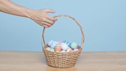 Wall Mural - Hand holding basket full of colorful Easter eggs on blue background. Easter holiday decorations concept.