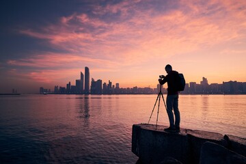 Wall Mural - Silhouette of photographer with tripod. Young man photographing urban skyline. Abu Dhabi at dawn, United Arab Emirates