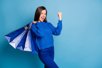 Poster - Photo of crazy excited girl hold bags raise fists with shopping bags isolated over blue color background