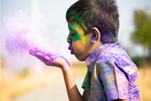 Kid Blowing Holi Colour Powder From Hand During Holi Festival Celebration - Concept Of Young Kids Having Fun By Playing Holi During Festive.