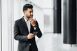 © Тарас Нагирняк - Handsome bearded Indian businessman at work in the office center, a young Indian, he holds a phone in his hand and speaks through headphones