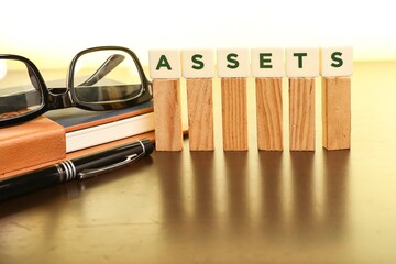 Asset management concept.  Block letters on Assets on the wooden sticks with a pen, and eyeglasses on the notebook