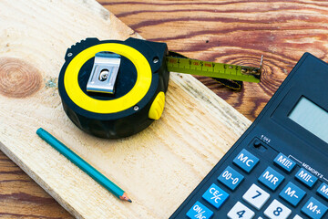 construction meter-tape measure calculator for calculations pencil and wooden board are on the workbench