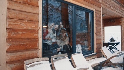 Women, best friends spending winter vacation in wooden mountain house. Drinking hot beverages and gossiping near the big window. High quality photo