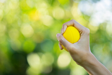 Hands of a woman squeezing a yellow stress ball with green background