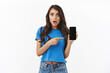 © Cookie Studio - Worried and shocked, startled young woman say something hideous online, showing smartphone screen with disturbed, frustrated expression, pointing mobile display, standing white background