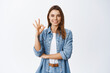 © Cookie Studio - Portrait of confident woman showing alright OK sign and looking satisfied, approve good thing, praise and recommend product, standing on white background