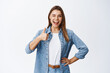 © Cookie Studio - Cheerful young woman with blond hair and casual clothes, showing thumb up in approval, like good thing, approve and recommend it, praise nice job or saying yes, white background