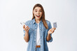 © Cookie Studio - Portrait of excited blond girl shopping online on smartphone, holding credit card and smiling amazed, standing over white background