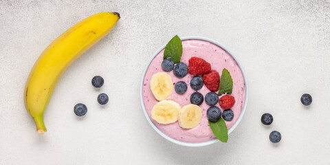 Wall Mural - Smoothie bowl with banana and berries on grey background. Top view. Healthy food concept