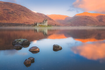 Wall Mural - Scottish Highlands landscape of the historic ruins of Kilchurn Castle reflected on a calm, peaceful Loch Awe with sunset or sunrise golden light.