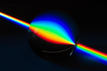 A Rainbow streak of light traveling in the darkness and being inverted by the reflection on a glass marble